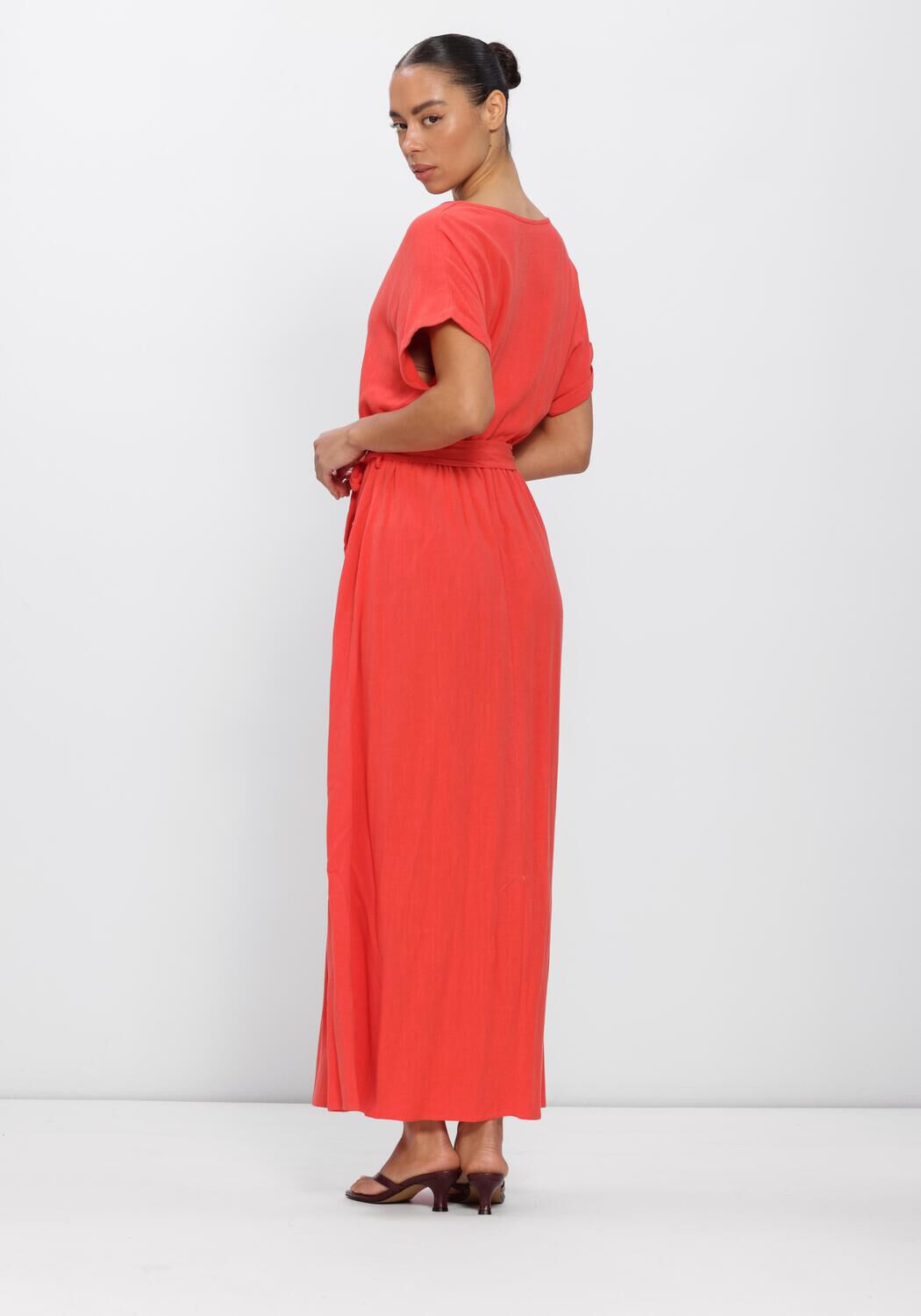 Pink Baby Alina belted wrap maxi dress in coral fabric, featuring a flowing silhouette and waist tie detail.