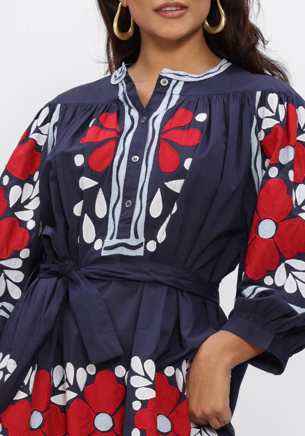 Pink Baby Elena navy floral embroidered midi dress displayed on a hanger with detailed embroidery and flowing fabric.